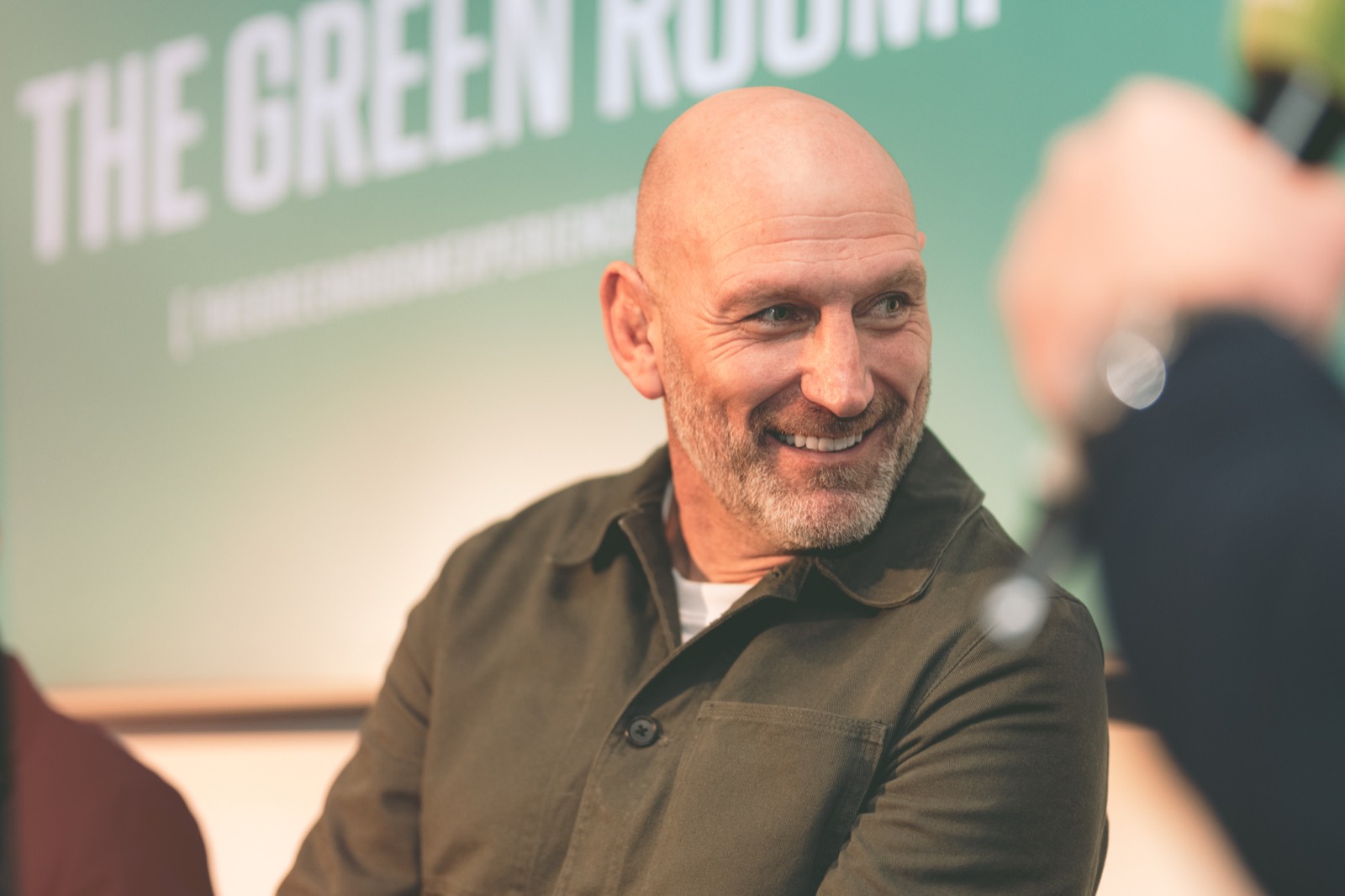 Green Room host smiling in front of the branded backdrop.